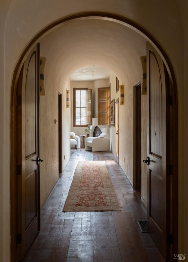 hall with arched walkways, dark wood-style flooring, and visible vents