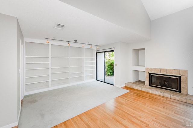 unfurnished living room featuring baseboards, a tiled fireplace, visible vents, built in shelves, and wood finished floors
