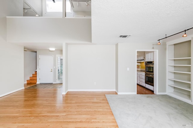 unfurnished living room featuring stairway, track lighting, visible vents, light wood-style floors, and a textured ceiling