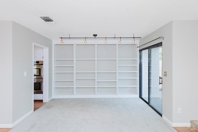 unfurnished room featuring rail lighting, visible vents, light carpet, baseboards, and built in shelves