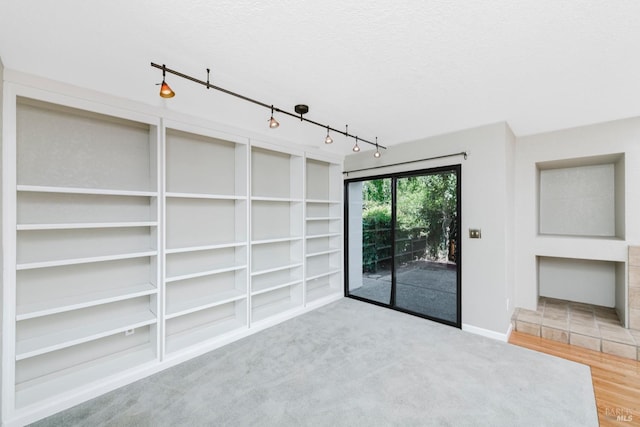 interior space featuring rail lighting, baseboards, built in features, and a textured ceiling
