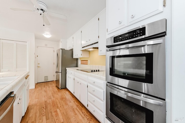 kitchen with light wood-style flooring, white cabinetry, under cabinet range hood, stainless steel appliances, and tile counters