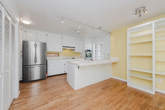 kitchen featuring tile countertops, a peninsula, white cabinetry, under cabinet range hood, and stainless steel appliances