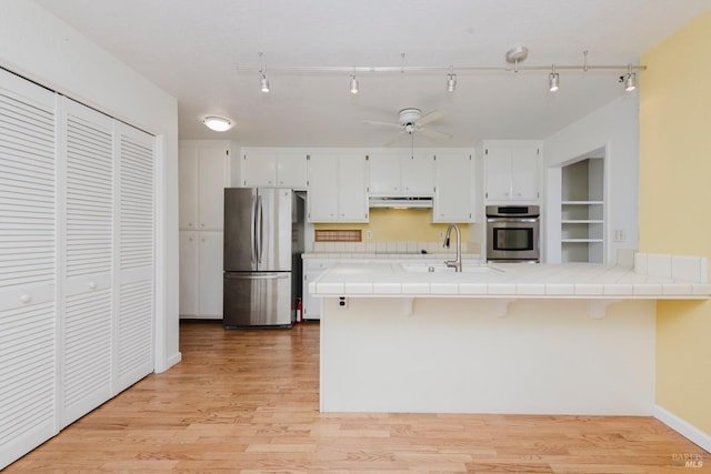 kitchen featuring ceiling fan, appliances with stainless steel finishes, under cabinet range hood, white cabinetry, and tile countertops