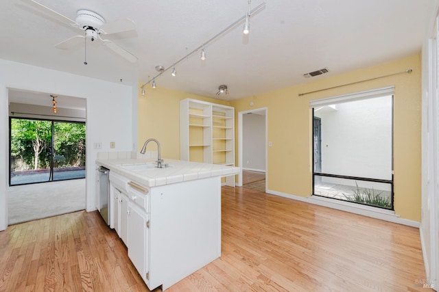 kitchen with a peninsula, white cabinets, visible vents, tile countertops, and a sink