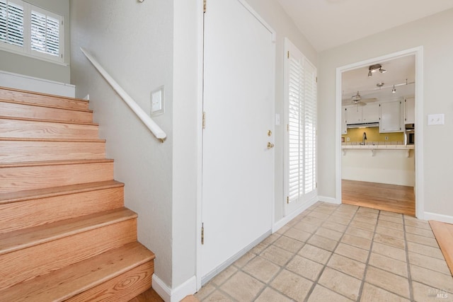 staircase featuring track lighting, ceiling fan, baseboards, and tile patterned flooring