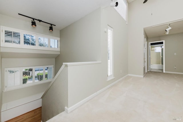 hallway with plenty of natural light, an upstairs landing, baseboards, and track lighting