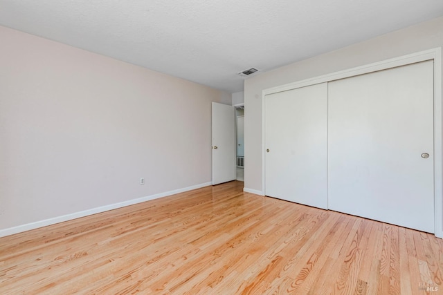 unfurnished bedroom featuring a closet, visible vents, baseboards, and wood finished floors