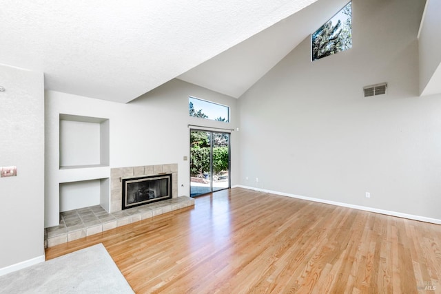 unfurnished living room featuring high vaulted ceiling, a fireplace, visible vents, wood finished floors, and baseboards