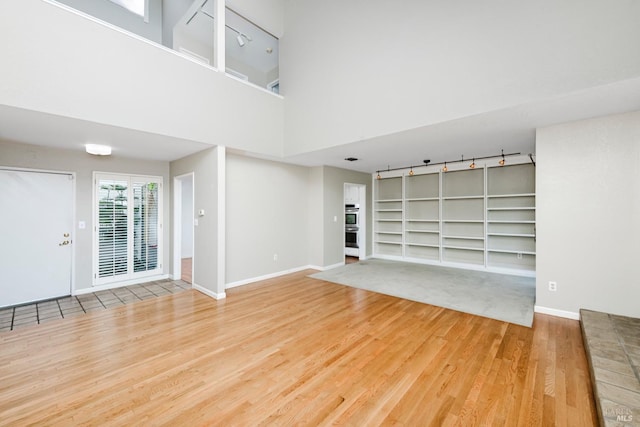 unfurnished living room with baseboards, rail lighting, wood finished floors, and built in shelves