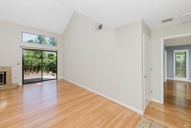 unfurnished living room featuring baseboards, a fireplace, light wood-style flooring, a high ceiling, and visible vents