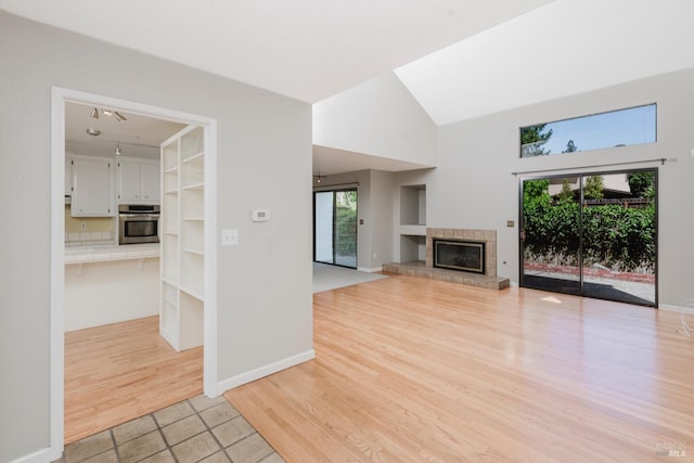 unfurnished living room featuring baseboards, light wood-type flooring, a high ceiling, and a tile fireplace