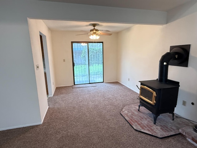 interior space featuring baseboards, a wood stove, ceiling fan, and carpet flooring