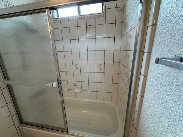 bathroom with bath / shower combo with glass door and a textured wall