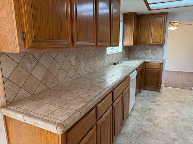 kitchen featuring tile counters, stone finish floor, brown cabinetry, and a sink