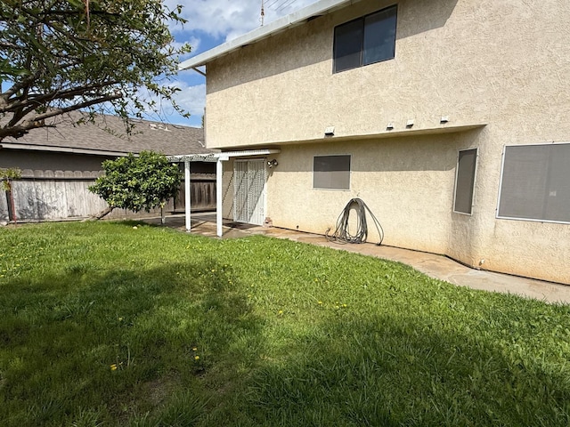 rear view of house featuring a lawn, fence, and stucco siding