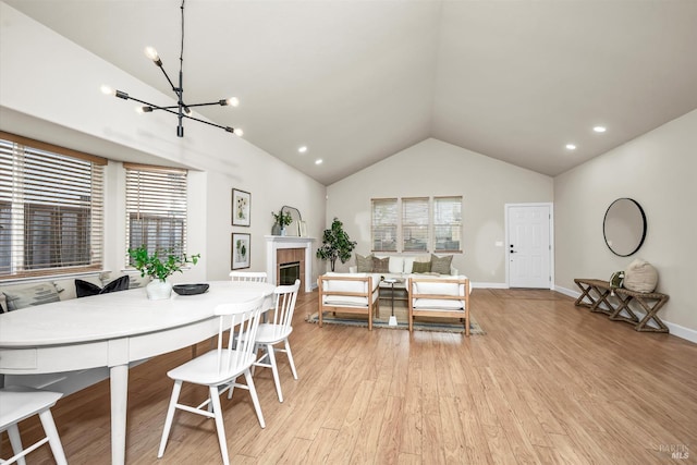 dining area with a tiled fireplace, a chandelier, light wood-type flooring, lofted ceiling, and baseboards