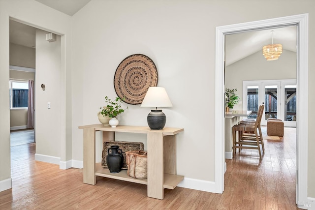 corridor with vaulted ceiling, baseboards, a chandelier, and wood finished floors