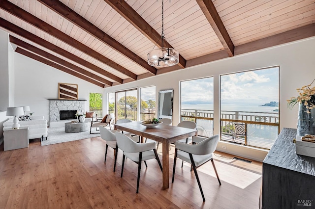 dining area featuring wooden ceiling, a fireplace with raised hearth, a notable chandelier, vaulted ceiling with beams, and wood finished floors