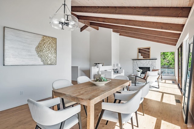 dining area featuring a notable chandelier, wood ceiling, vaulted ceiling with beams, a stone fireplace, and light wood-type flooring