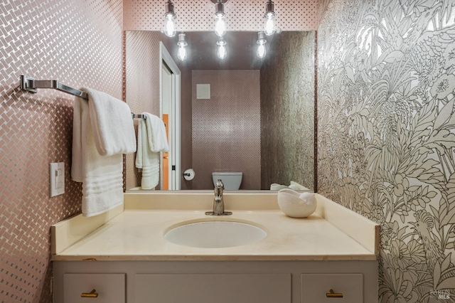 bathroom with toilet, vanity, and wallpapered walls