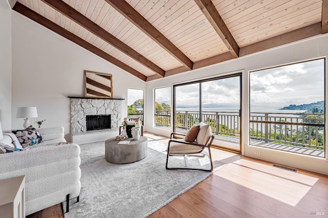 living area with wood ceiling, wood finished floors, a stone fireplace, visible vents, and beamed ceiling