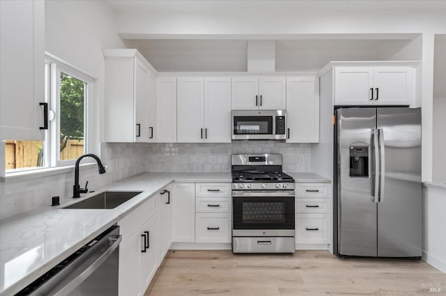 kitchen with a sink, stainless steel appliances, backsplash, light stone counters, and white cabinetry