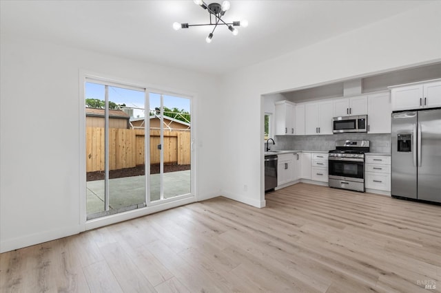 kitchen featuring light wood-style flooring, a sink, appliances with stainless steel finishes, light countertops, and a notable chandelier