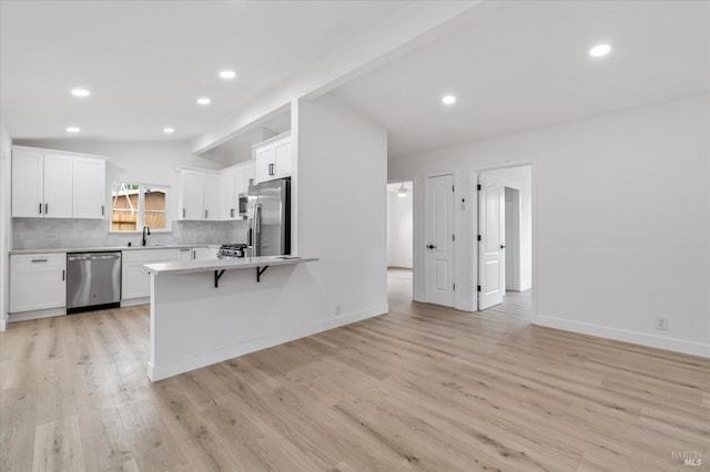 kitchen with lofted ceiling, stainless steel appliances, light wood-style flooring, and white cabinets