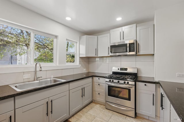 kitchen featuring stainless steel appliances, recessed lighting, dark countertops, a sink, and backsplash