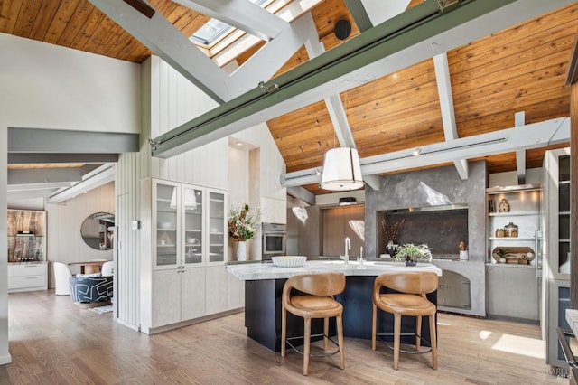 kitchen with light wood-style flooring, a skylight, beamed ceiling, and oven
