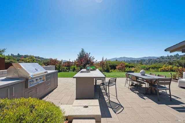 view of patio / terrace with a grill, outdoor dining space, a sink, a mountain view, and an outdoor kitchen