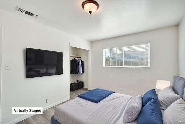 bedroom with baseboards, a closet, wood finished floors, and visible vents