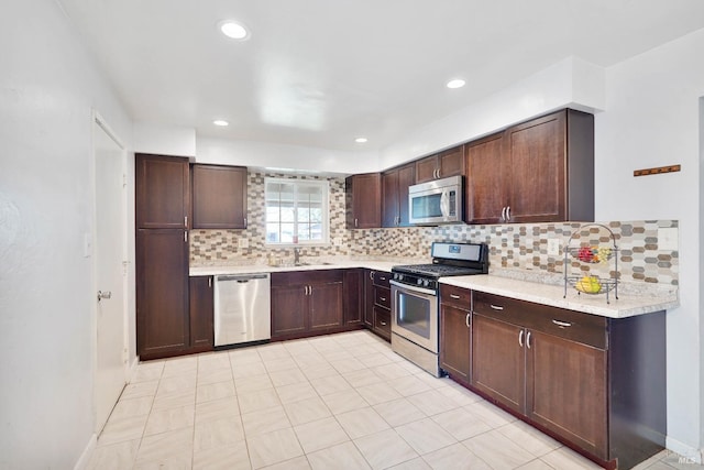 kitchen with dark brown cabinets, appliances with stainless steel finishes, a sink, light countertops, and tasteful backsplash