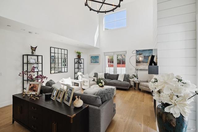 living area with a high ceiling, baseboards, light wood-style flooring, and a notable chandelier