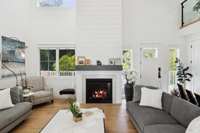 living area featuring wood finished floors, a towering ceiling, and a glass covered fireplace