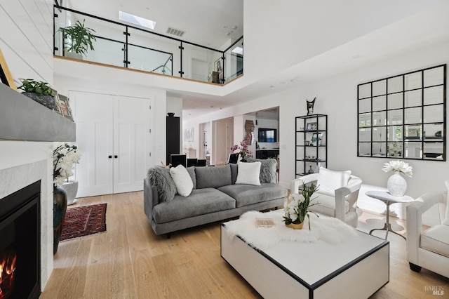 living area featuring light wood finished floors, a lit fireplace, visible vents, and a towering ceiling