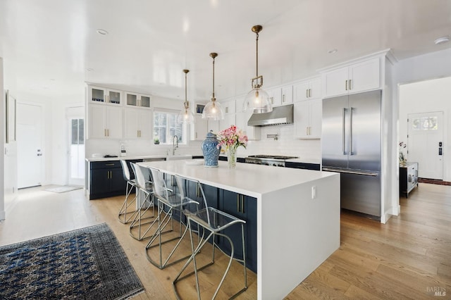 kitchen featuring light wood-type flooring, under cabinet range hood, stainless steel built in fridge, and a kitchen island