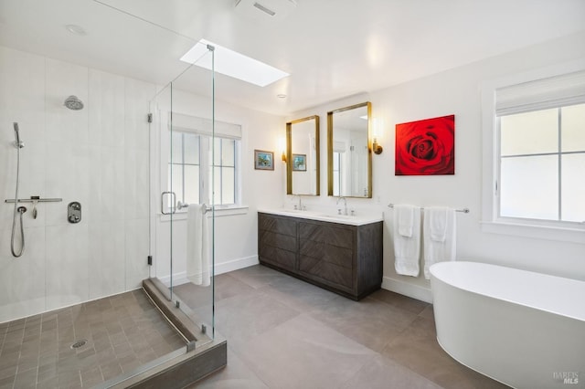 full bathroom featuring a sink, a skylight, a stall shower, a freestanding bath, and double vanity
