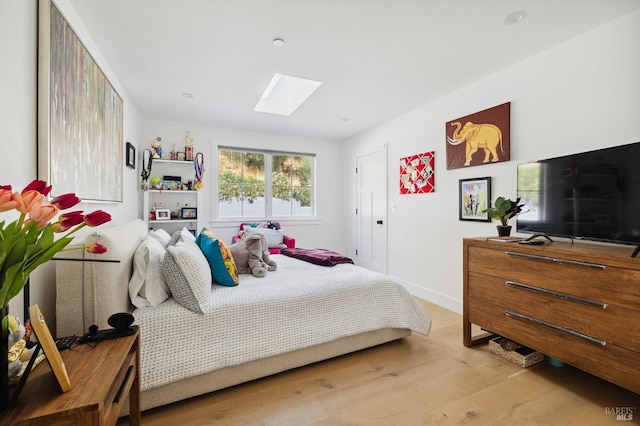 bedroom featuring a skylight, baseboards, and wood finished floors