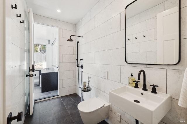 full bathroom featuring tile walls, a tile shower, toilet, tile patterned floors, and a sink