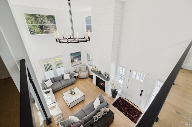 living room featuring a warm lit fireplace, a notable chandelier, a high ceiling, and wood finished floors