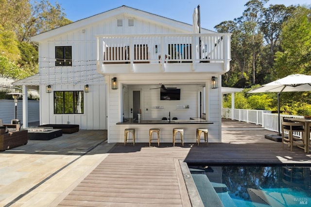 back of property featuring outdoor dry bar, board and batten siding, a balcony, a deck, and an outdoor fire pit