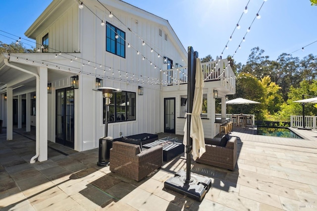 back of property with an outdoor hangout area, an outdoor pool, a patio area, and board and batten siding