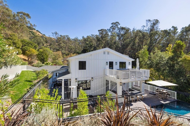 back of property featuring a fenced in pool, a deck, board and batten siding, a fenced backyard, and outdoor dining space