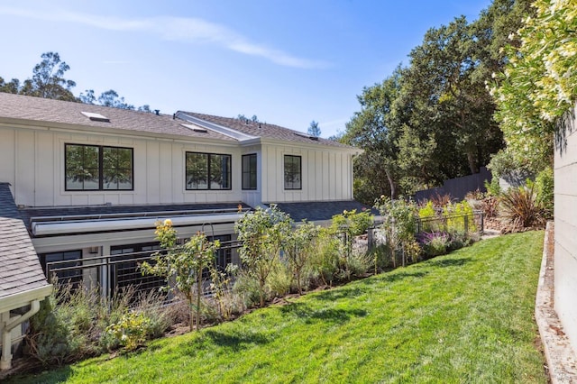 rear view of house featuring a lawn, fence, and board and batten siding