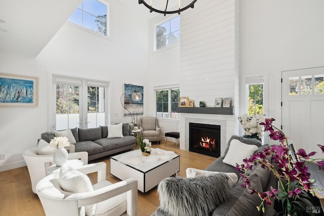 living area featuring a lit fireplace, a towering ceiling, and light wood finished floors