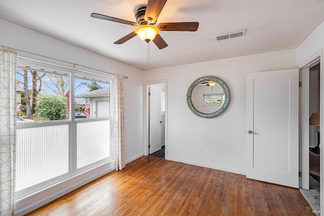 unfurnished room featuring wood finished floors, visible vents, a ceiling fan, and baseboards