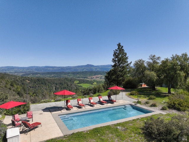 outdoor pool featuring a wooded view, a mountain view, and a patio area