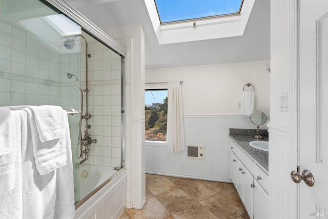 bathroom featuring a skylight, vanity, a wainscoted wall, shower / bath combination with glass door, and heating unit